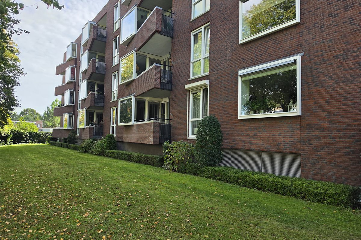 Foto ter illustratie: een appartementencomplex van baksteen met balkons en een gemeenschappelijke tuin.
