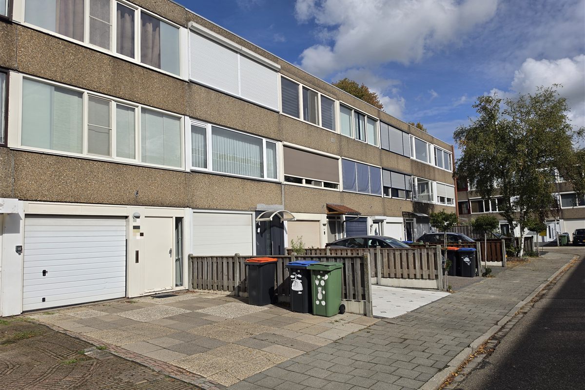 Foto ter illustratie: een rij tussenwoningen (rijtjeshuizen) uit de jaren zeventig, met garages op de begane grond.